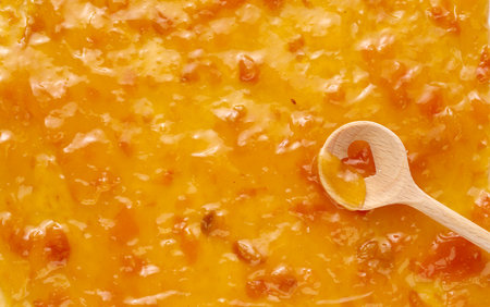 From above of wooden spoon with heart shaped hole and sweet orange apricot jamの写真素材