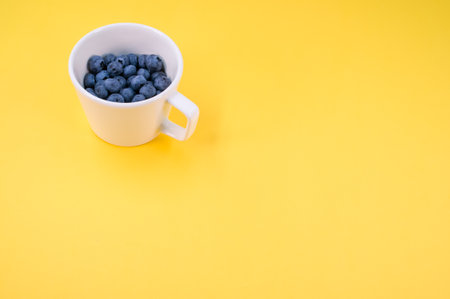 view of sweet tasty blueberries on a plate on a yellow background with text space