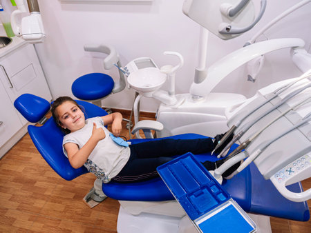 Little Caucasian girl is smiling, lying on the dental clinic chair and making the ok gesture with her hand.の写真素材