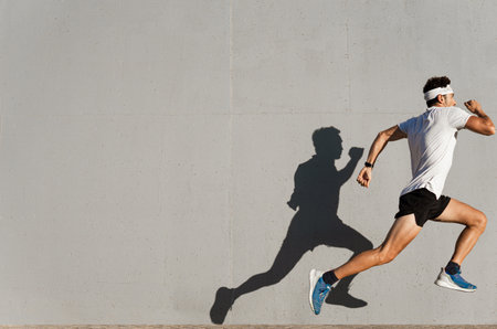 Caucasian young man doing sport jumping, shadow cast on the wallの写真素材