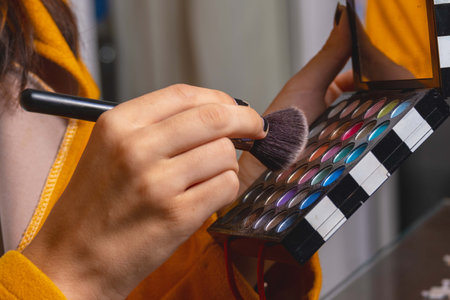 Detail shot of the hands of a woman holding a set of eyeshadows and makeup brushの写真素材