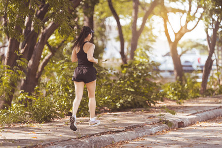 Happy smiling adult Asian woman jogging outdoor in the city park in sunshine beautiful summer day. ...
