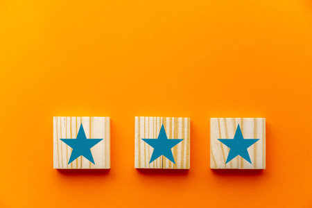 On a orange backdrop, a three-star sign is depicted on wooden cubes. Concepts such as customer experience, satisfaction survey, evaluation, increase rating, and top outstanding services rating.の写真素材
