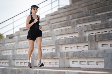 A healthy adult Asian woman running up on concrete stairs of the city stadium to strengthen bodyの写真素材