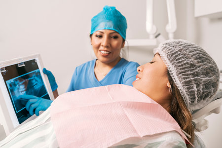 Dentist in uniform and protective gear pointing an X-ray to a patient lying on the stretcher clinicの写真素材