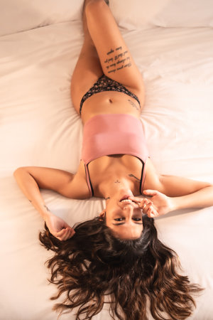 Lifestyle, sexy brunette Caucasian girl in pink pajamas lying on the bed looking at cameraの写真素材