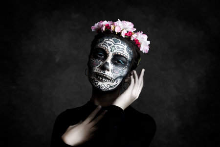 Woman with face painted as a Catrina and flowers in her hair on dark background. Day of the Deadの写真素材