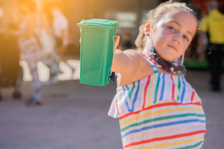Close-up of a green garbage container held by a Caucasian girl. Selective focus.の写真素材