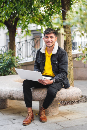 Latin man sitting on a stone bench in the park with laptop looking at cameraの写真素材