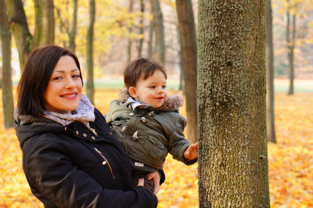 Woman holding a two years old boy at a park in the autumnの写真素材