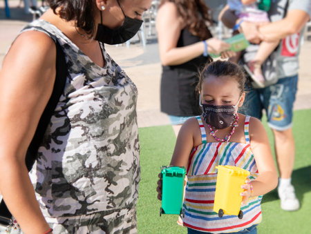 Caucasian girl with mask showing a woman the green and yellow garbage cans. Recycling concept.