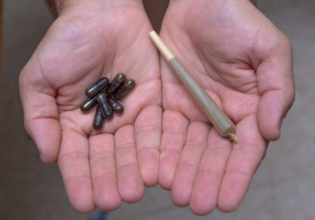 Close-up of a man's hands holding pills in one and a cannabis joint in the other. Concept of therapeutic cannabis, medical cannabis, legalization of cannabisの写真素材