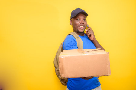 An African dispatch man with back pack, making a call, carrying boxes and wearing a face capの写真素材