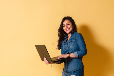 Portrait of happy young woman holding laptop smiling look camera over yellow background.の写真素材