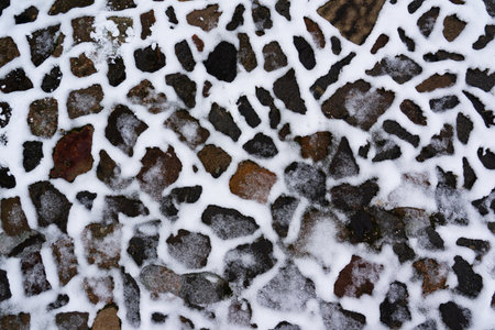 A path of different natural stones is partially covered with snow, winter texture for wallpaper and design, concept of winter and snowfallの写真素材