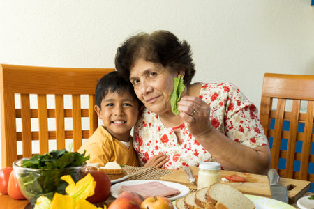 portrait of a little boy with his grandmother, in a kitchen, hugging while smiling and looking at the cameraの写真素材