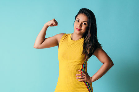 young latinx woman looking at camera showing arms muscles, power girl concept.の写真素材