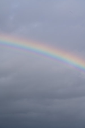 Colorful rainbow in front of a thick dark cloud cover, rain clouds and stormsの写真素材