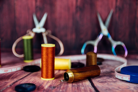 Front view of orange and green yarn spools. In the background vintage sewing scissors on red...