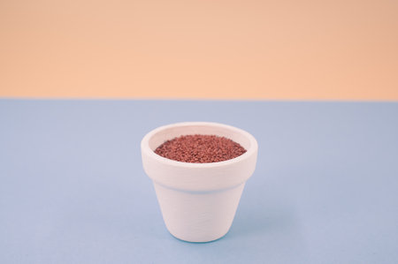 white vase filled with terracotta color decorative sand on white background with space for textの写真素材