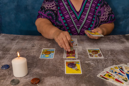 older white-haired woman reading tarot cards on a wooden table with candleの写真素材