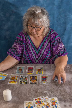 older white-haired woman reading tarot cards on a wooden table with candleの写真素材