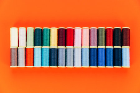 Multicolored sewing threads arrange like rainbow. Top view. Orange backgroundの写真素材