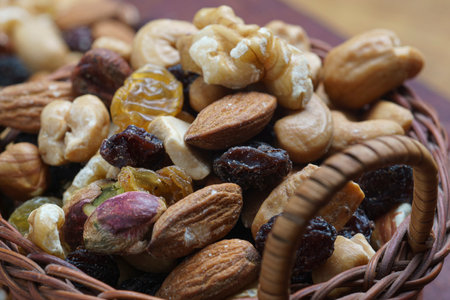 close view of basket with dried fruits (pistachio, raisins, almonds, peanuts, walnuts) on wooden boardの写真素材