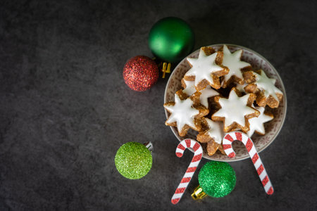 A cup with Christmas biscuits on black background and green and red Christmas baublesの写真素材