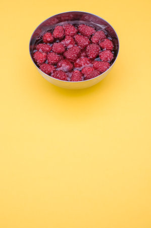 sweet tasty raspberries in a bowl filled with water on yellow background and copy spaceの写真素材