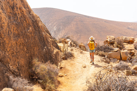 A girl hiker with a yellow backpack on the Mirador de la PeÃ±itas trail in the PeÃ±itas canyon, Fuerteventura, Canary Islands. Spainの写真素材