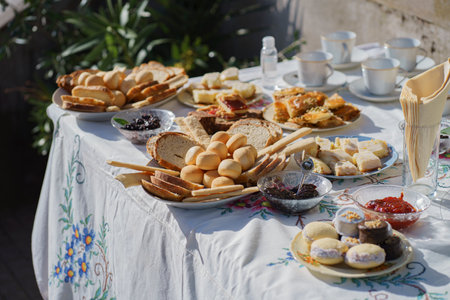 Table decorated for an outdoor celebration with crockery, food, and arrangement on white tablecloth
