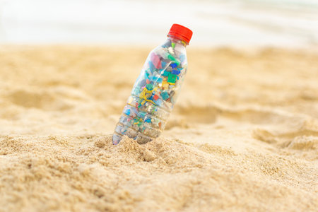 Bottle filled with microplastics collected from the sea lying on the sand of the beach.の写真素材
