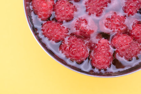sweet tasty raspberries in a bowl filled with water on yellow background and copy spaceの写真素材