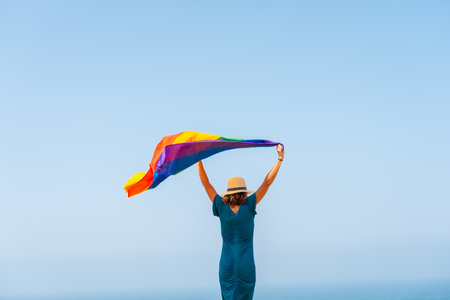 Lgbt symbol, an unrecognizable lesbian person with his back turned, waving the flag and the blue sky in the background, icon of homoxesualityの写真素材