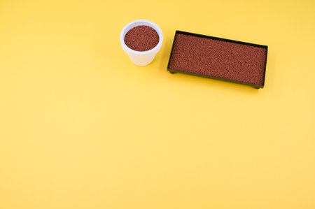 a metal box and vase filled with terracotta color decorative sand on yellow background with space...