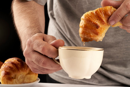 man's hands dipping sweet croissants in tea or coffee cupの写真素材