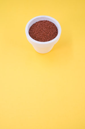 white vase filled with terracotta color decorative sand on yellow background with space for textの写真素材
