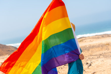 An unrecognizable lesbian person in a green dress and with the LGBT flag by the sea, symbol of homosexualityの写真素材