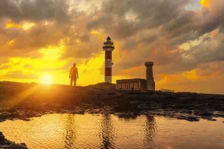Silhouette of a young man in the cloudy sunset of the Toston Lighthouse, Punta Ballena near the town of El Cotillo, Fuerteventura island, Canary Islands. Spainの写真素材