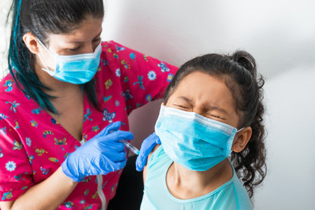 children's nurse injecting brown girl's arm. doctor injecting covid-19 vaccine. girl closes her eyes...