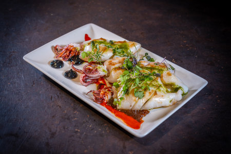 Fried squid with sauce on a black background, on a white plate