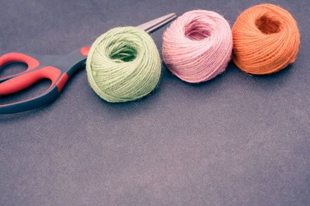 multicolor decoration yarns with scissors on a dark stone background with copy space