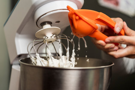 Unrecognizable person using squeezer to squeezing a lemon into the bowl of a mixer for the...