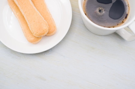 black coffee in a mug and plate with savoiardi biscuits on a white background with copy spaceの写真素材