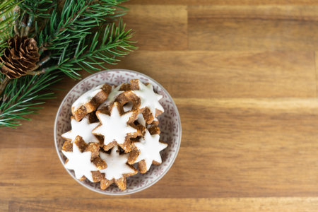 A cup with christmas biscuits on a wooden table and with fir branches, top view