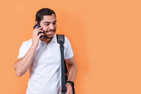 Happy bearded student talking on the phone, with handbag on his shoulder.の写真素材