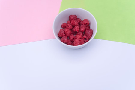 sweet tasty raspberries in a bowl on multicolored background and copy space