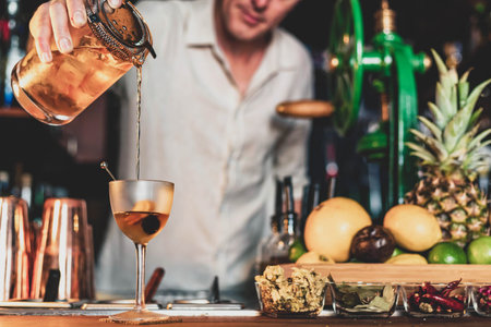 A professional bartender pouring a cocktail in a glass from a shaker and mixer, view of a barman...