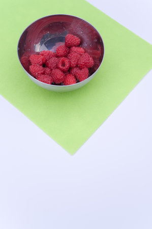 sweet tasty raspberries in a bowl on multicolored background and copy space